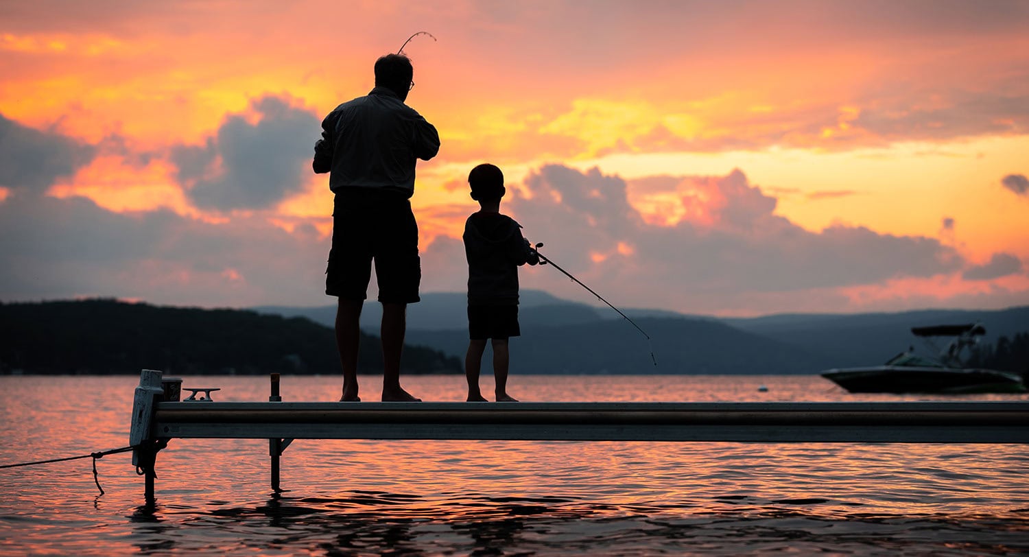 Father and son fishing on a dock during a colorful sunset.