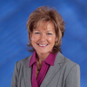 Professional woman in gray blazer and purple blouse smiling for a portrait.