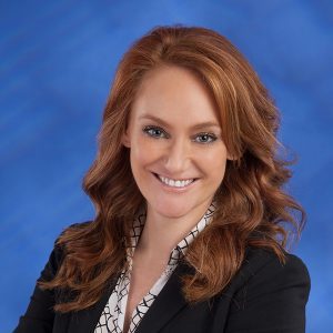 Professional woman with red hair smiling, wearing a black blazer and patterned blouse.