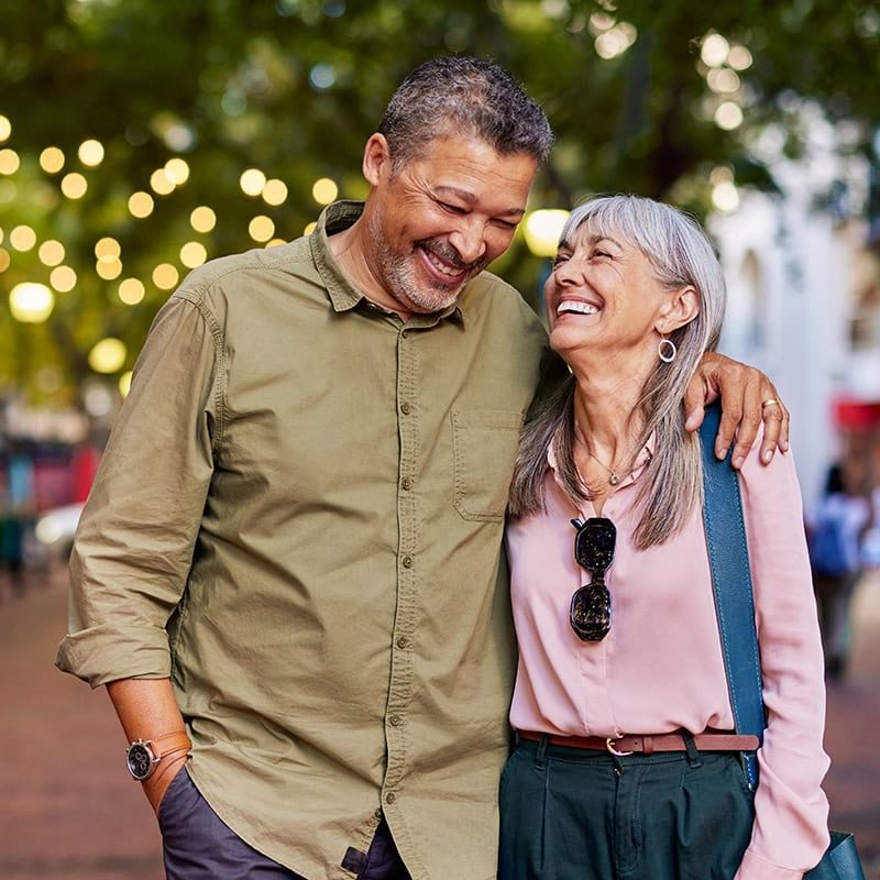 Happy senior couple enjoying outdoor evening with string lights and trees in background.